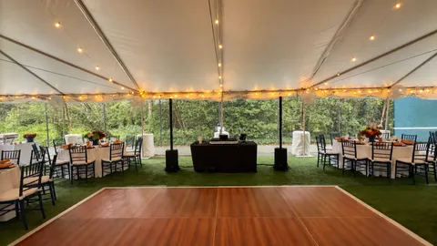 Tented reception setup with a wood dance floor, DJ station, and warm string lights